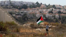 Un palestino agita su bandera ante una colonia Un palestino agita su bandera ante una colonia