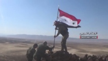 Unos soldados ponen la bandera siria.