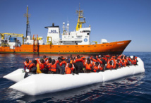 Una lancha con inmigrantes africanos y, detrás, el barco de SOS Méditerranée