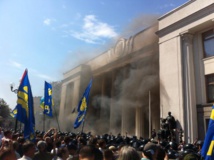 El humo de la granada sube, entre los manifestantes y los policías, delante del parlamento