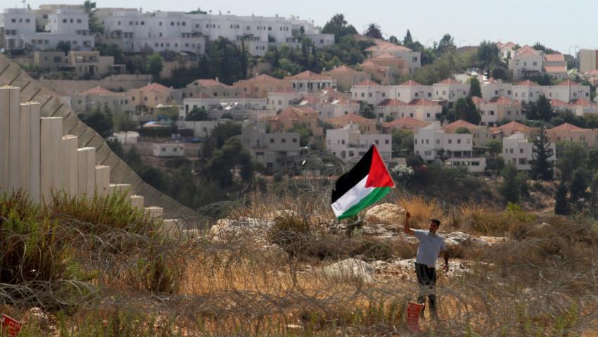 Un palestino agita su bandera ante una colonia