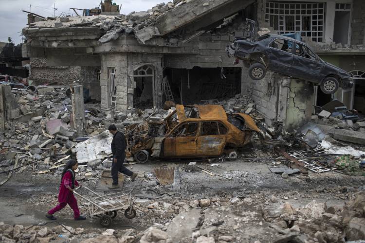 Gente andando al lado de coches destrozados en un barrio liberado de Mosul