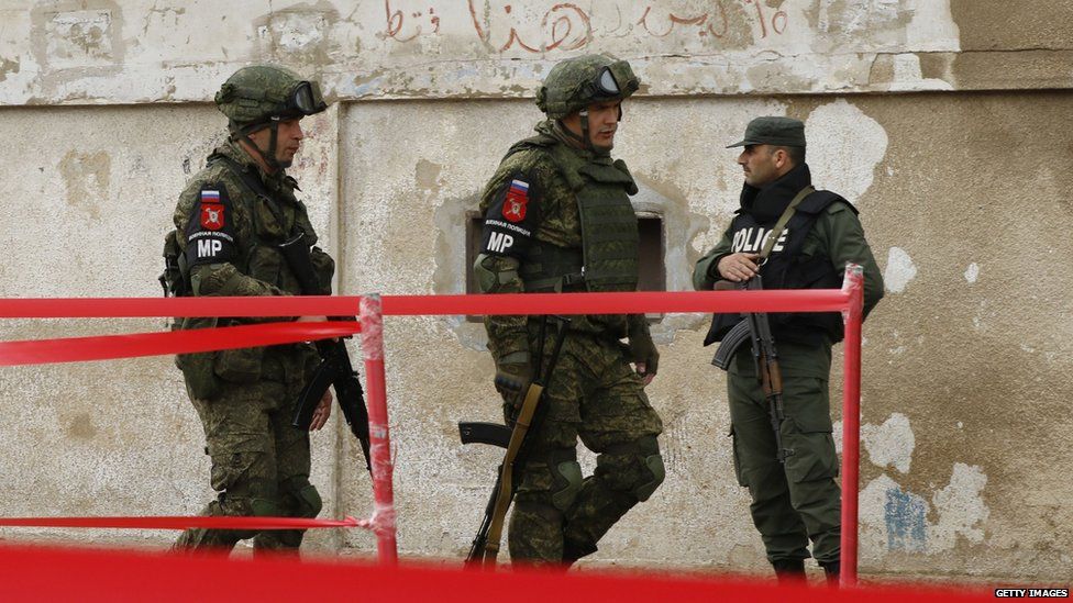 Policías militares rusos pasan al lado de un soldado sirio en Homs. Es probable que Rusia despliegue a su policía militar en las zonas de desescalada.