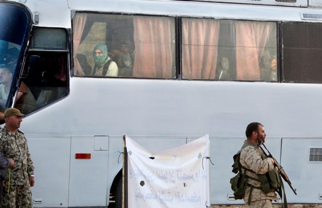 Un autobús con miembros de An Nusra pasa al lado de milicianos de Hizbolá que vigilan