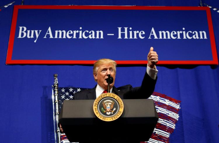 Trump habla ante un cartel donde pone: Compra americano- contrata americano