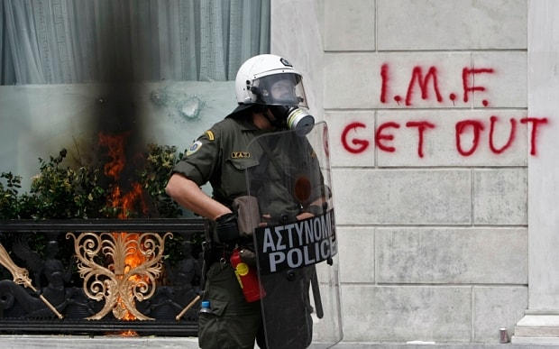 Un policía griego ante una pintada que dice "Vete FMI"