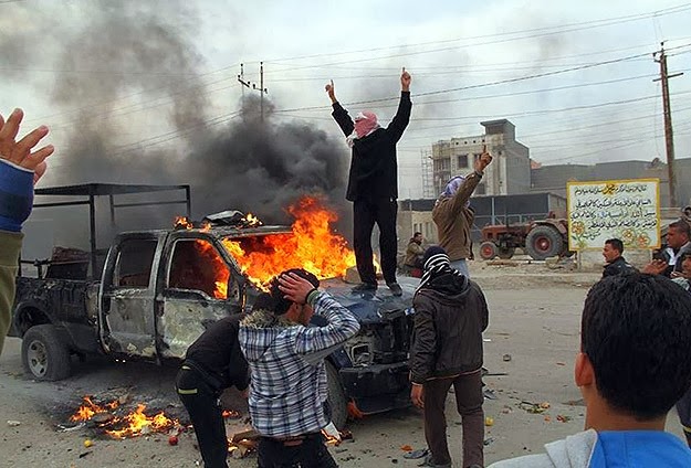 Un hombre encima de un coche de policía ardiendo, en Ramadi.