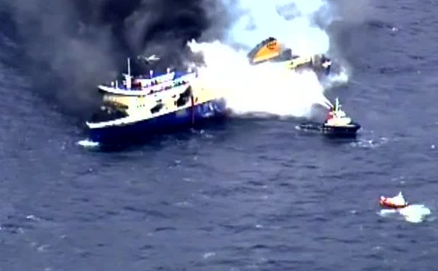 Un pequeño barco lanza agua al barco incendiado Un pequeño barco lanza agua al barco incendiado